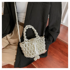 Détail du sac seau en perles avec noeud en soie blanche et bandoulière en perles élégante