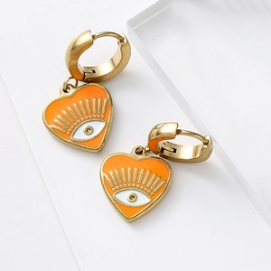 Detail of golden heart earrings with orange enamel evil eye charms on acrylic blocks