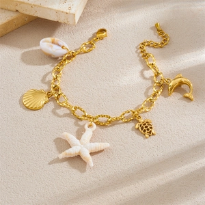 Gold bohemian star and seashell charm bracelet displayed on a textured beach stone surface