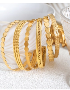 Detail of 18k gold plated stainless steel bangles with heart and textured patterns