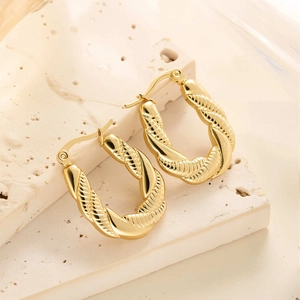 Gros plan de boucles d'oreilles créoles ovales en acier titane doré 18 carats torsadées