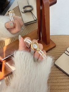 Detail of vintage oval gold watch with pearl bracelet strap on a warm textured background