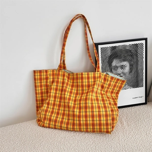 Detail of red and yellow plaid canvas tote bag leaning against a minimalist white wall