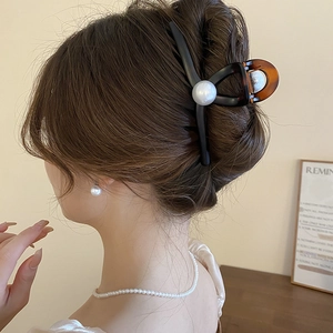 Detail of tortoiseshell acrylic hair claw with large pearl on brown hair for women