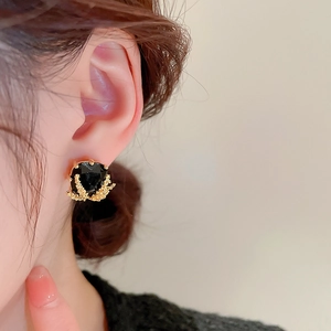 Close-up of black zircon stud earring with golden wheat motif on earlobe