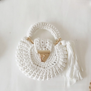 Detail view of a white crochet round bag with gold clasp and elegant fabric tassel