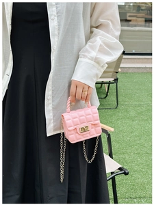 Close-up of pink quilted jelly bag with gold chain and clasp held in hand outdoors