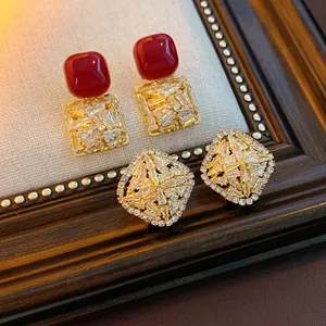 Square and rhombus earrings with red stones and gold plating on textured fabric