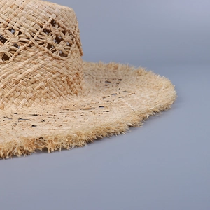 Detailed macro view of woven raffia sun hat with hollow lace pattern and frayed brim edge