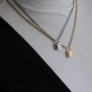 Detail of interlocking gold and silver lock pendants on flat Cuban chains worn with a blazer