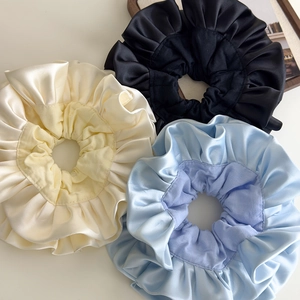 Close-up of three satin scrunchies in black, beige, and blue with ruffled texture