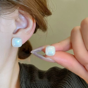 Macro shot of square pearl stud earrings with iridescent luster on female model ear