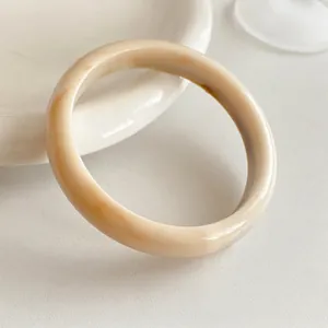 Minimalist cream resin bangle with marble texture on a white decorative ceramic tray