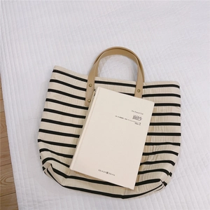 Top-down view of black and white striped canvas tote with brown leather handles and rivets
