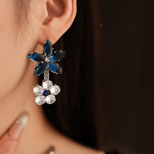 Close-up of silver floral earrings with dark blue and clear zircon on model's ear