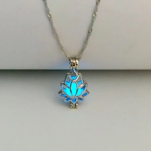 Close-up of a silver lotus locket necklace glowing with an intense blue light