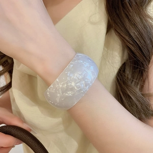 Detailed view of broad acrylic iridescent eye bangle featuring marble textures on wrist