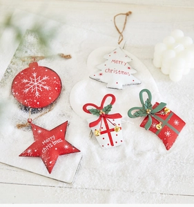 Detail of five metal Christmas ornaments with red stars and trees on snowy wood base