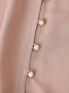 Dettaglio della camicia in raso rosa con bottoni dorati tondi e trama del tessuto