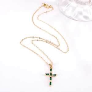 Detail of gold cross necklace featuring baguette-cut green zircons and simple cable chain