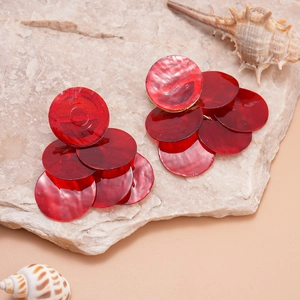 Macro detail of layered red resin round discs earrings on a textured stone background