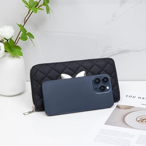 Black quilted long wallet with gold butterfly clasp on marble surface holding smartphone