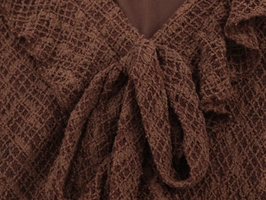 Detail view of the V-neckline with decorative bow tie and intricate lace knitting