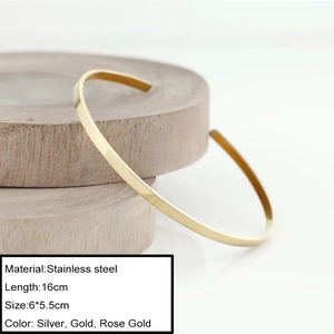 Minimalist stainless steel open bangle in gold finish displayed on a wooden stand