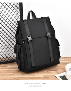 Front view of black flap backpack with buckle straps and side pockets on wooden desk