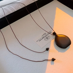 Macro detail of dark ebony wood pendant with vintage aesthetic and rustic string
