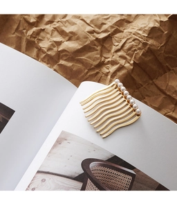 Detail of golden wave hair comb featuring white faux pearls on textured paper background