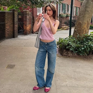 Outdoor street style view of a pink polka dot camisole top with casual blue jeans