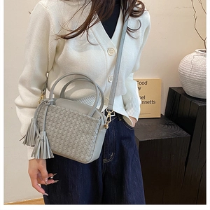 Detail of gray woven leather shoulder bag with tassels and adjustable strap on a model