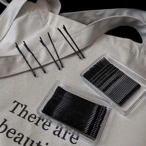 Close-up of black metal bobby pins set in clear storage cases on white canvas background