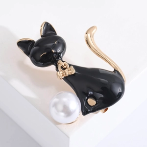 Detailed close-up of a black enamel cat brooch with a gold bow and white pearl accent