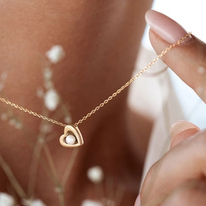 Close-up of golden heart pendant with center pearl on a female neck for elegant jewelry detail