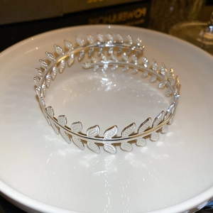 Macro detail of silver leaf-inspired open cuff bracelet on a white ceramic display tray