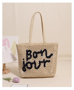 Close-up of woven straw tote bag with bon jour embroidery and rustic handles