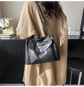 Dettaglio di una grande borsa tote nera in pelle con catena indossata su un trench