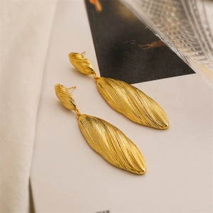 Close-up of long gold earrings featuring irregular wavy textures and a brushed metal finish