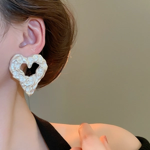 Macro shot of irregular cream white heart earrings with textured lava surface on ear