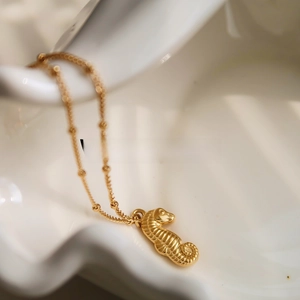 Macro shot of 18K gold plated seahorse pendant necklace on a wavy white ceramic plate