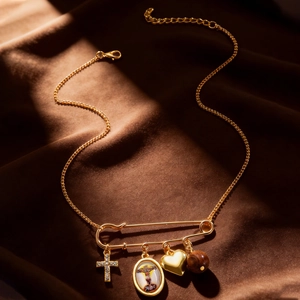 Detail of gold safety pin necklace with cross and heart charms on brown silk