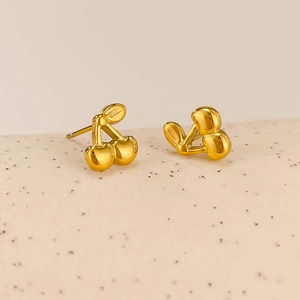 Macro shot of gold cherry stud earrings with smooth metallic finish and leaf detail