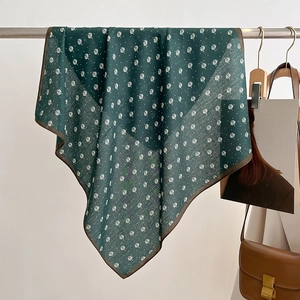 Close-up of green silk scarf featuring white leaf patterns and brown hem on a metal bar