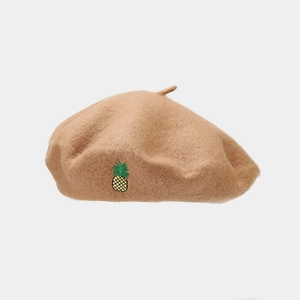 Détail du béret en laine avec broderie ananas sur un tissu en feutre beige doux