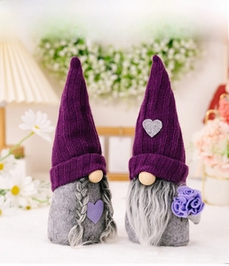 Detailed close-up of handmade purple knitted gnome plush with heart patch and floral decor