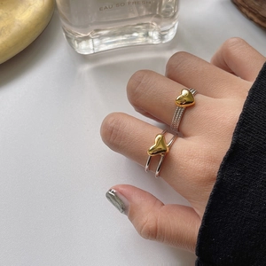 Detail of silver twisted heart rings and layered band worn by a model on a white table
