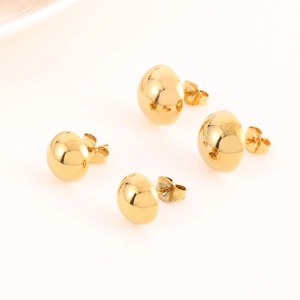 Macro shot of minimalist gold spherical stud earrings with polished mirror finish