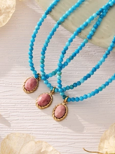 Close-up of turquoise beaded necklaces with pink stone evil eye pendants in gold setting
